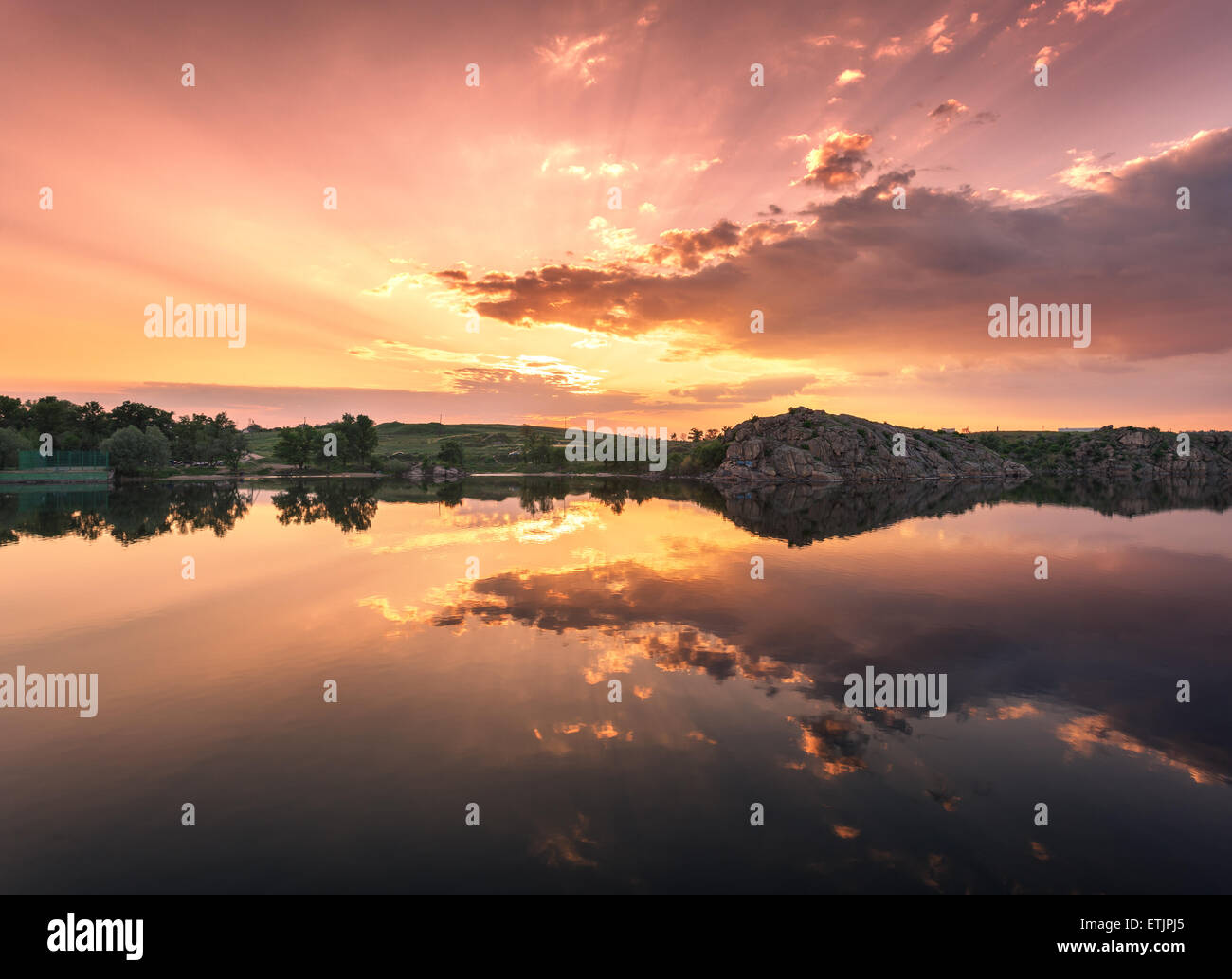 Beautiful summer sunset at the river with colorful sky, clouds, rocks grass and water with reflection. Ukraine Stock Photo
