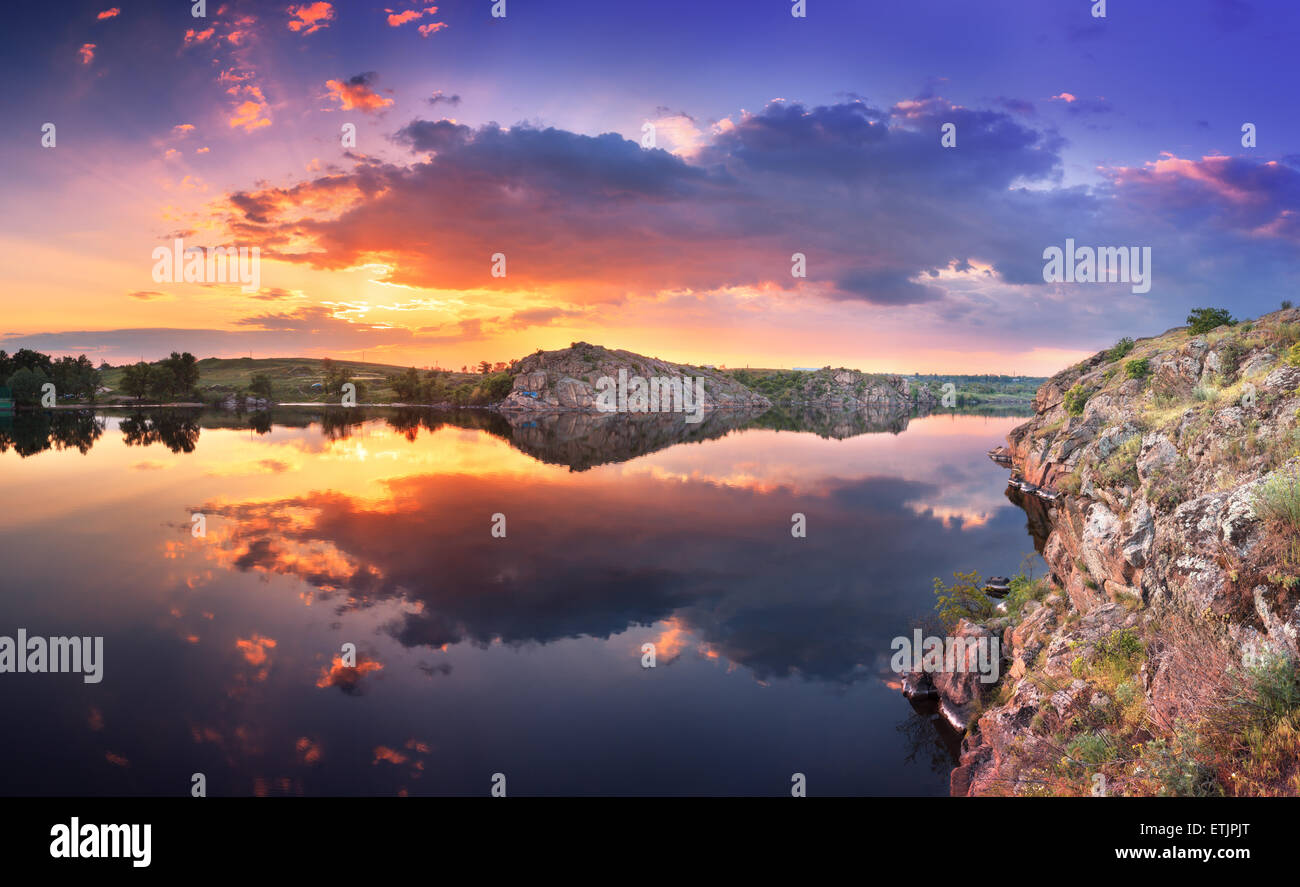 Beautiful summer sunset at the river with colorful sky, clouds, rocks grass and water with reflection. Ukraine Stock Photo