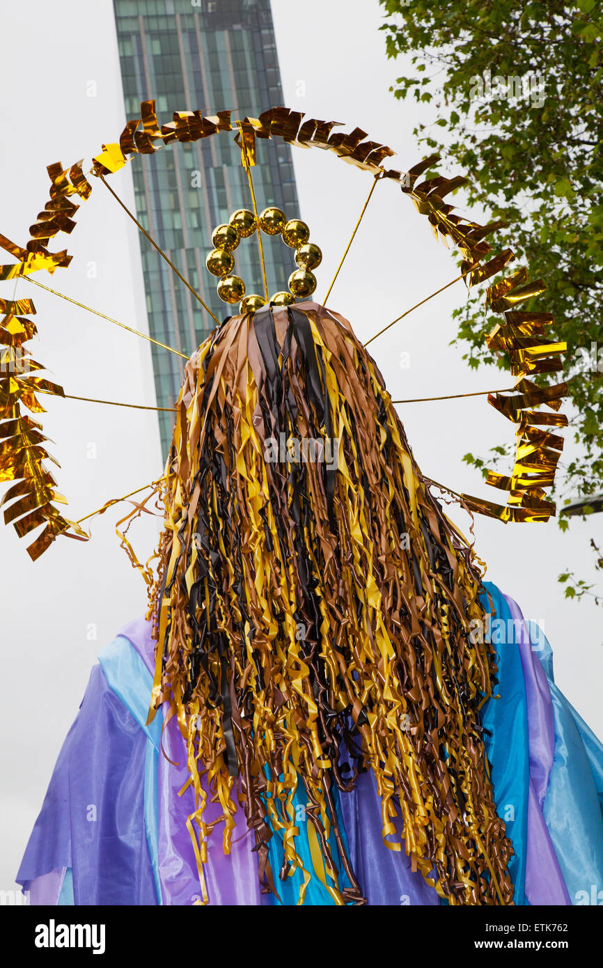 Gilded figure with long hair 'Looking up to the Hilton Hotel. Manchester Day was created in 2010 and has now become one of the North West’s flagship events of the summer. The purpose of the event is to celebrate the creativity and diversity of the city. Over 2,500 performers and artists from local communities bring streets and squares to life in a fantastic display of colour, sound and movement. Stock Photo