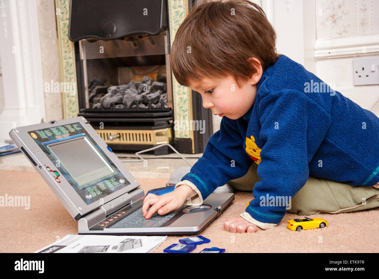 Young child, boy, 3-4 year old, indoors kneeling on carpet, playing intently with children's V-Tech laptop computer, learning basic computering skills Stock Photo