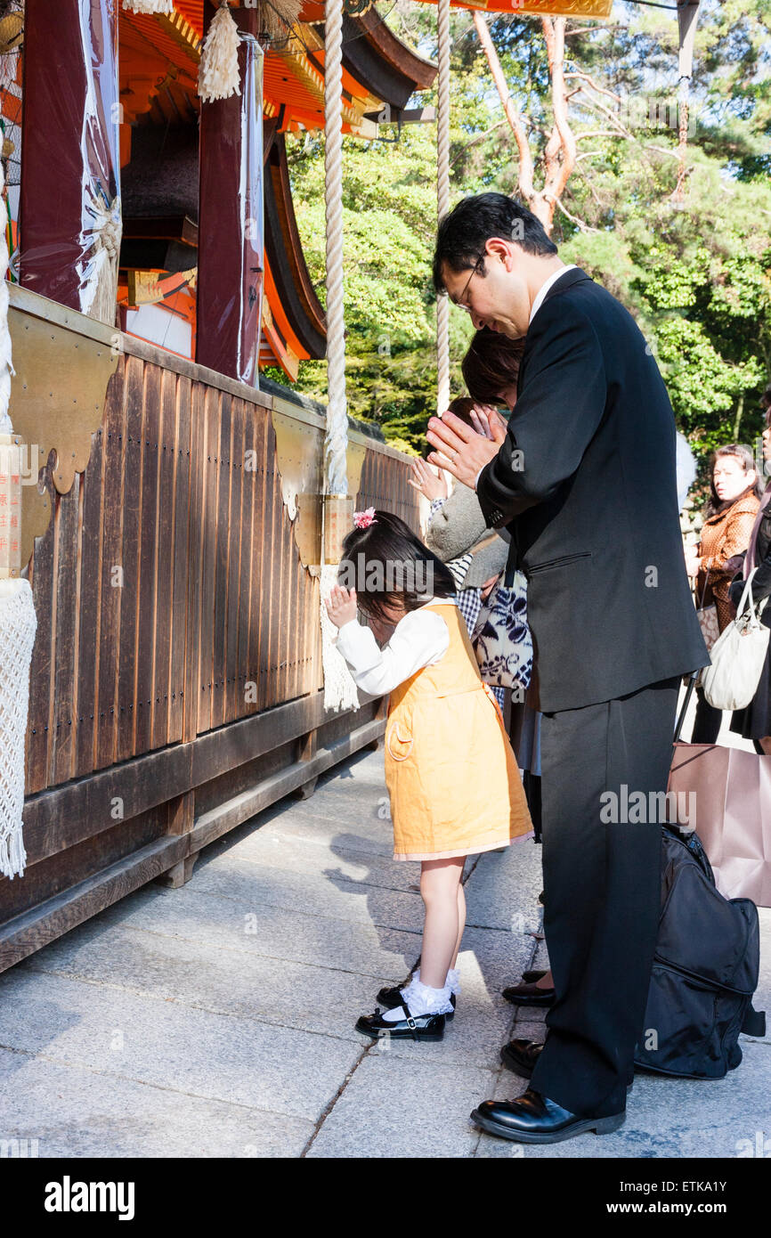 Yasaka shrine, Kyoto. Man in black suit, salaryman, and a little child, girl, both bowing and praying in front of the main hall, Gion-zukuri. Stock Photo