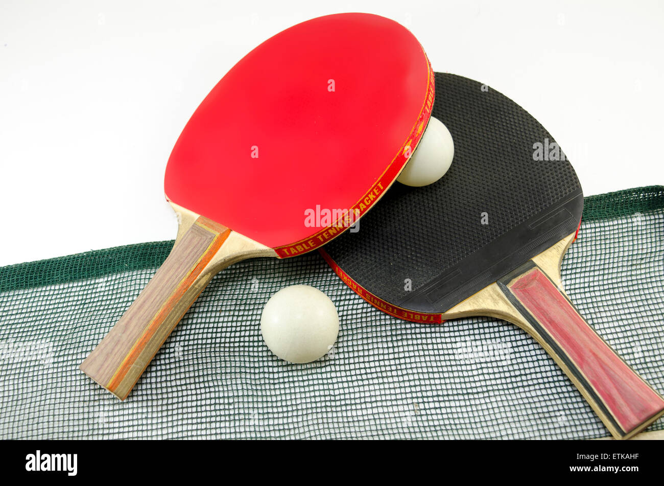 Two table tennis rackets one on top of the other and an old net isolated on white. One paddle is red and the other is black Stock Photo