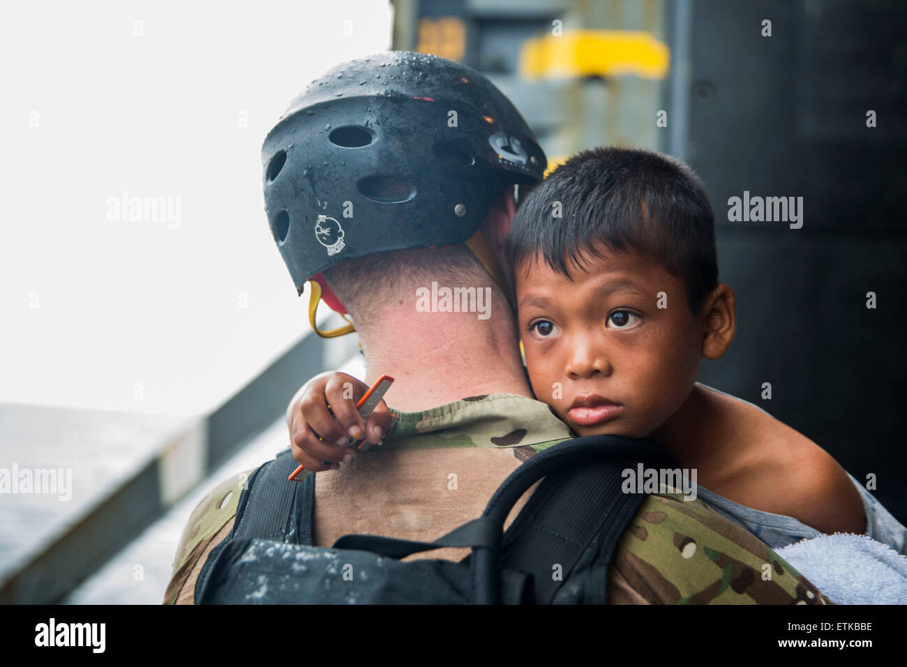 A US Navy Sailor carries a young Indonesian boy onto a watercraft to be transported to an Indonesian coast guard vessel from the USS Rushmore June 11, 2015 in the Pacific Ocean. The crew of the Rushmore rescued the group of refugees stranded between the Indonesian islands of Kalimantan and Sulawesi. Stock Photo
