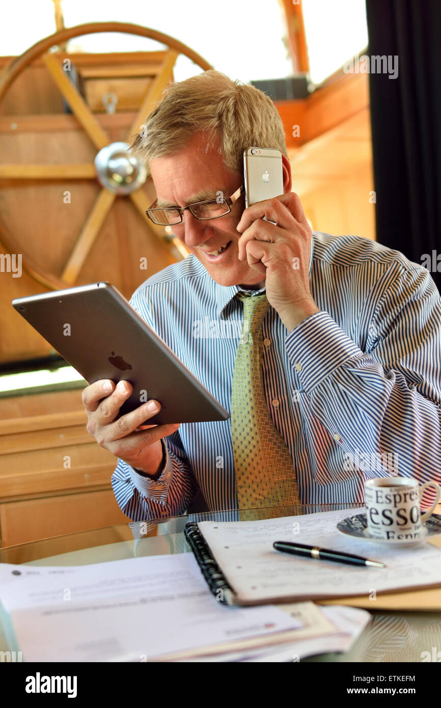 Online business meeting home alone businessman houseboat office at table with notes looking at iPad air tablet computer screen using iPhone smartphone Stock Photo