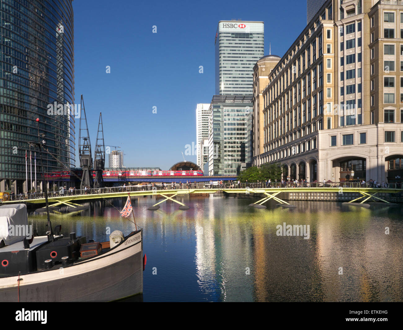Canary Wharf at North Dock with barge in foreground and HSBC building and West India Quay train cross rail tube rail station behind London E14 Stock Photo
