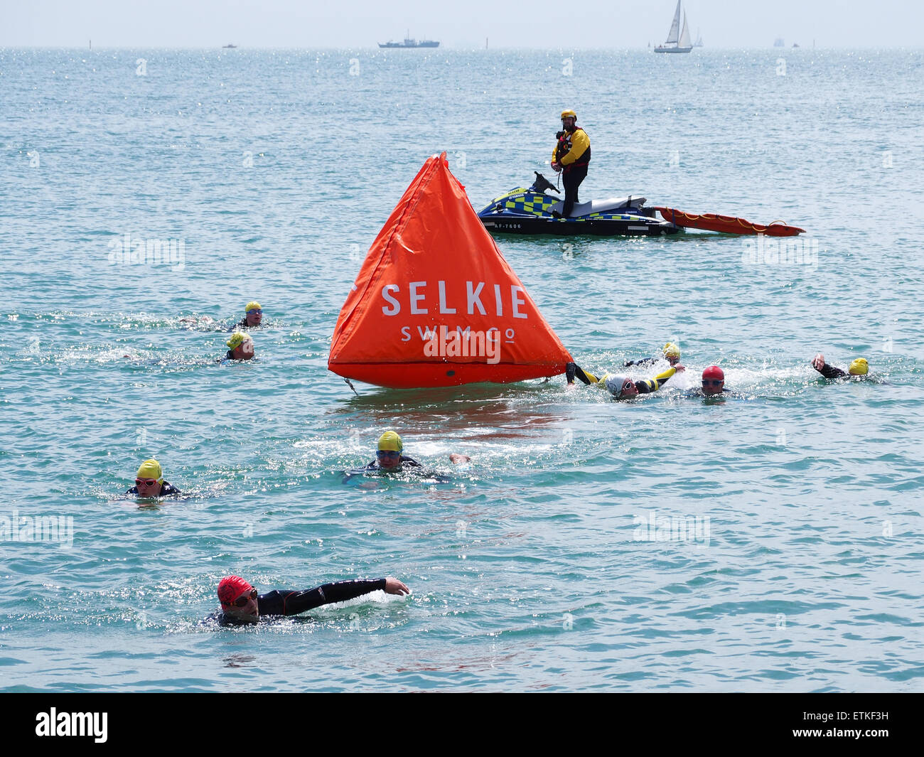 Competitors in a triathlon swim around a buoy in the Solent, watched over by a RLSS lifeguard on a jetski Stock Photo