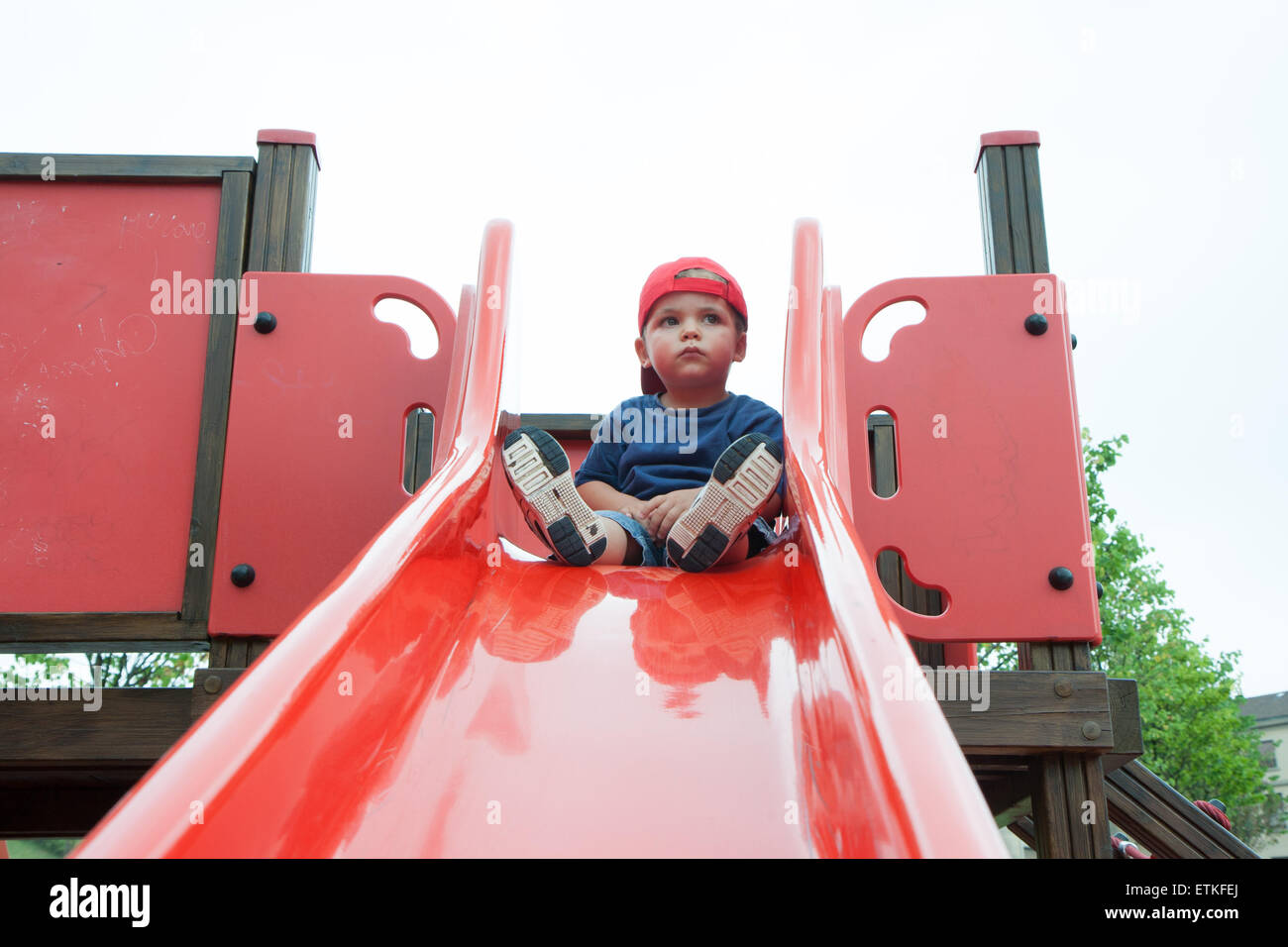 child with hat on red slide Stock Photo