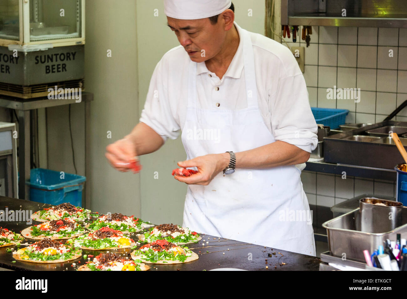 Japanese chef, preparing okonomiyaki on a hot plate in the kitchen of a