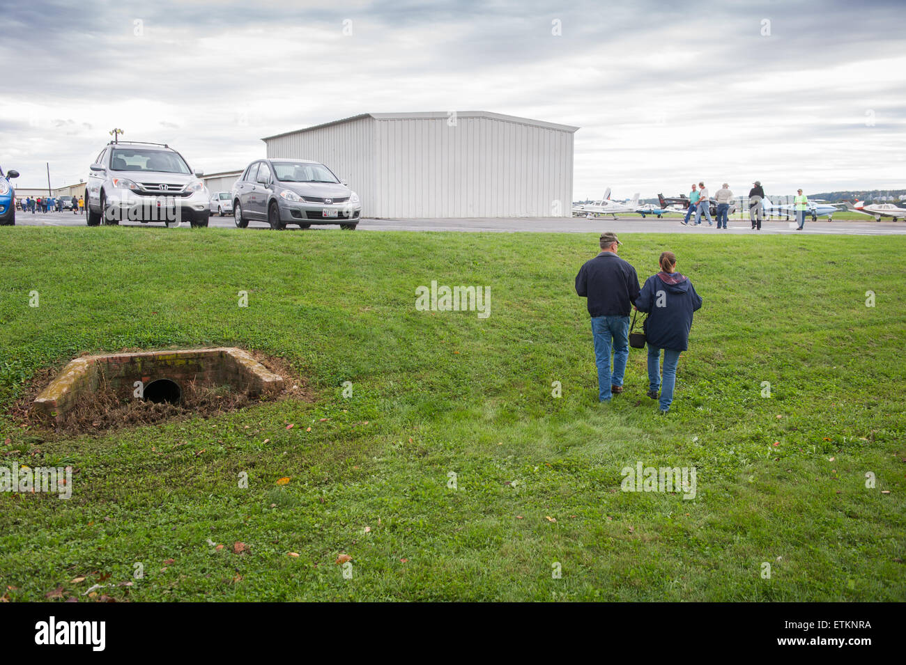 Couple walking up grassy hill towards small airplane hanger in Creswell, Maryland, USA Stock Photo