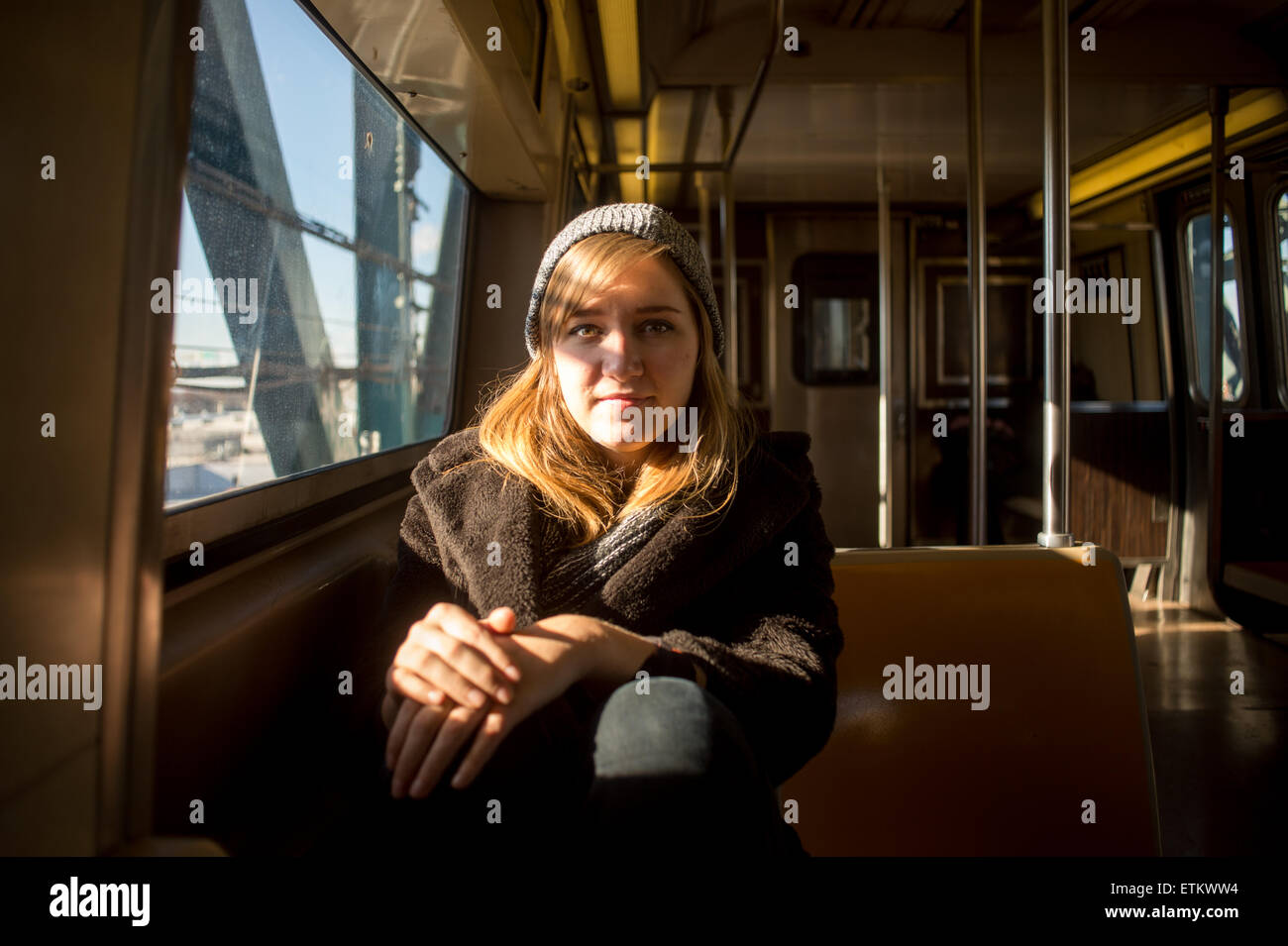 Young woman wearing a warm hat and coat sitting inside a subway train near New York, New York, USA Stock Photo
