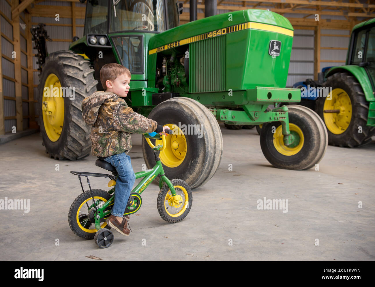 Young boy on John Deere bicycle in machine shed with tractors in Cordova, Maryland, USA Stock Photo