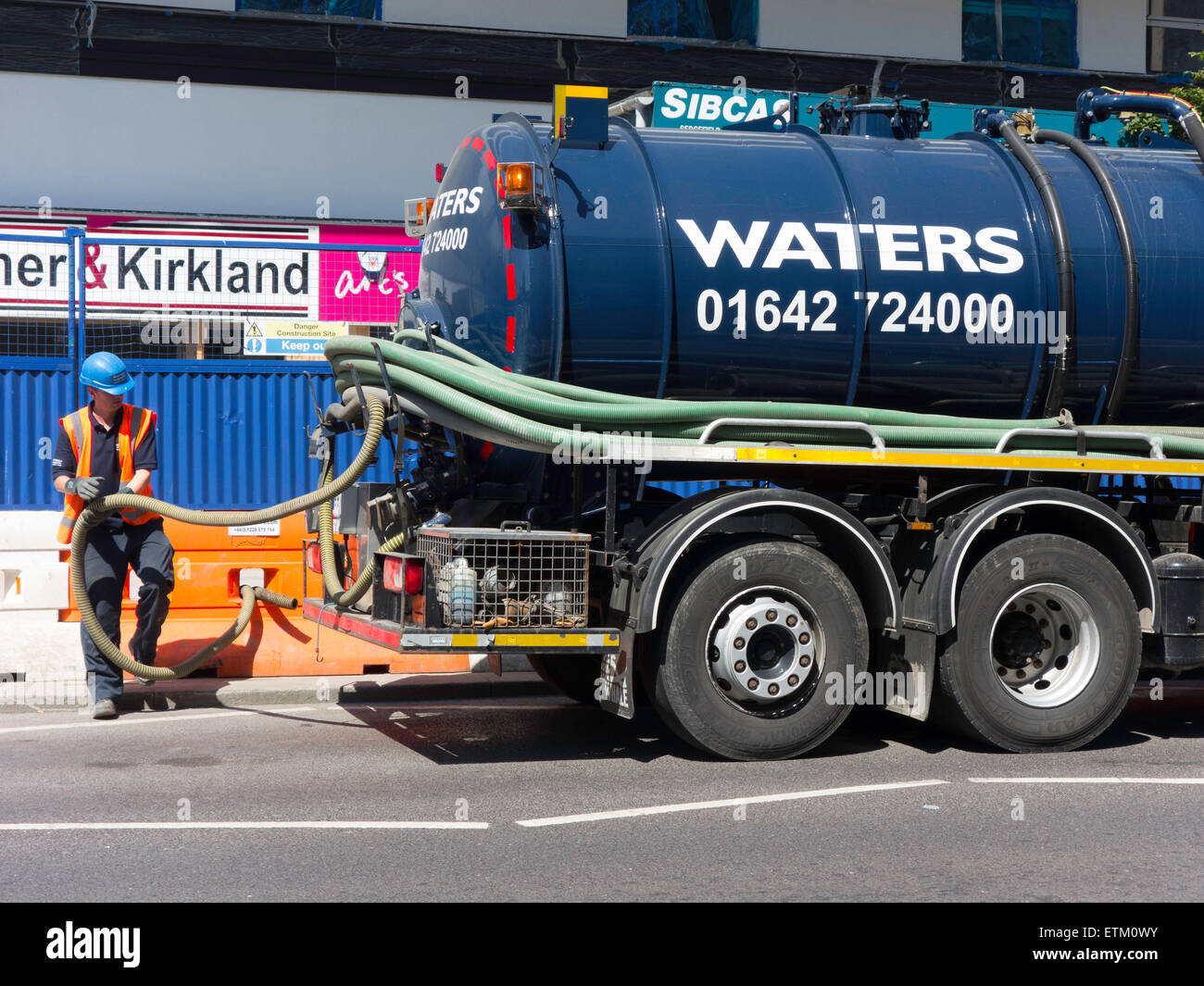 A waste water removal tank truck collecting waste from an Hotel construction site driver stowing hoses. Stock Photo