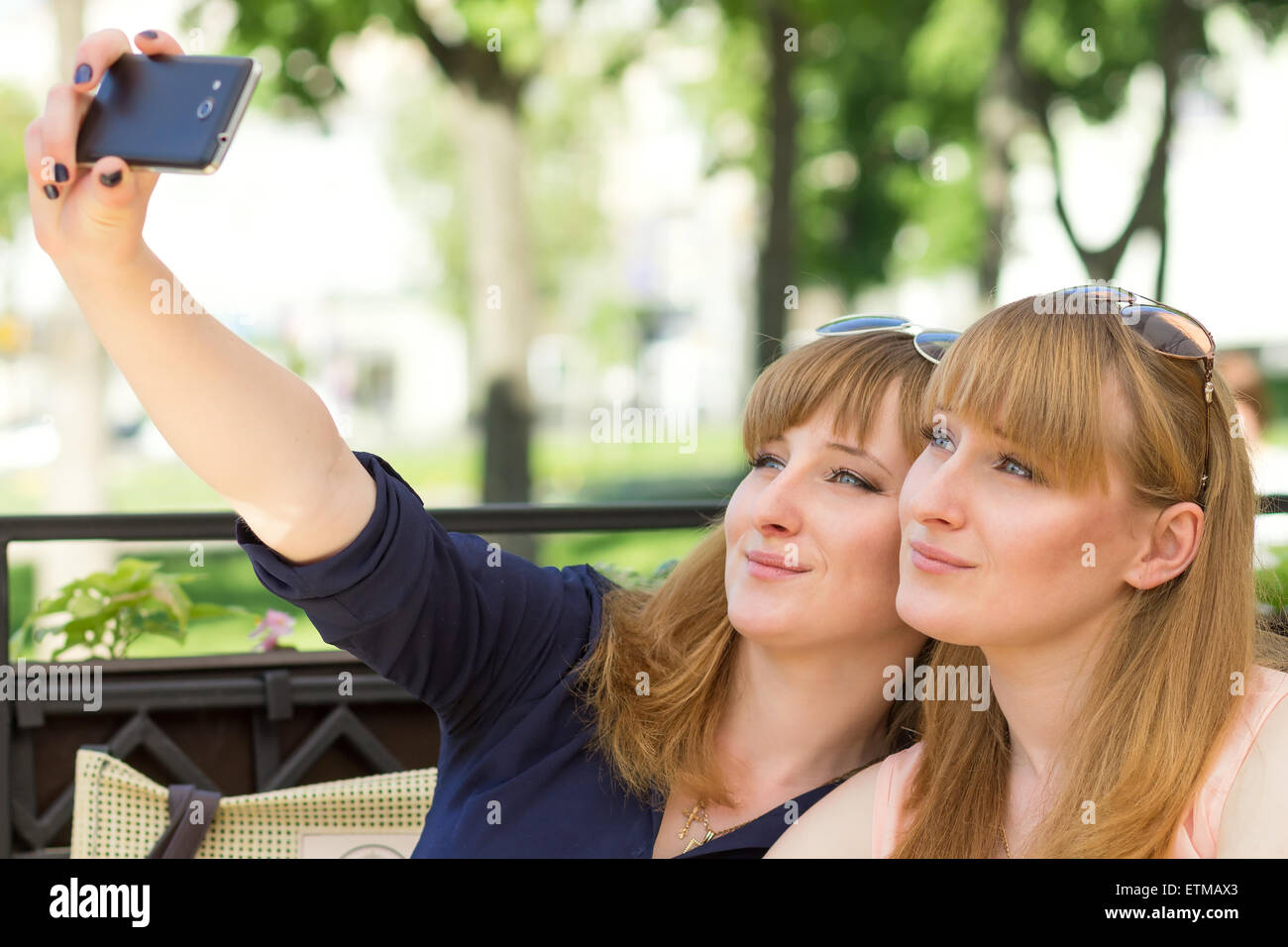 Two twins girls taking selfie in restaurant at sunny summer day. Young pretty sisters on terrace of cafe Stock Photo