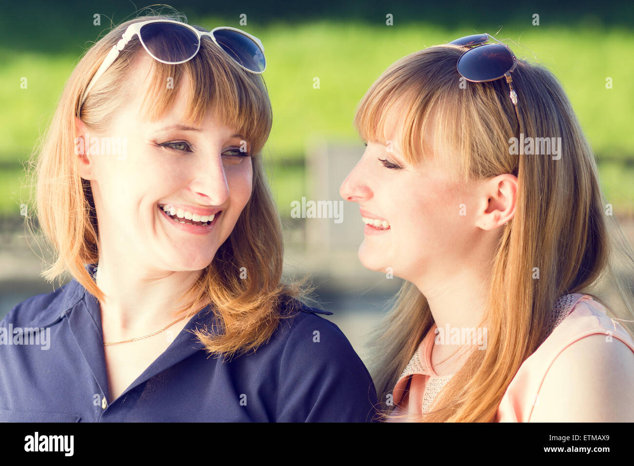 Young twins girls having fun laughing in summer park. Pretty students sister with sunglasses talking each other. Warm color tone Stock Photo