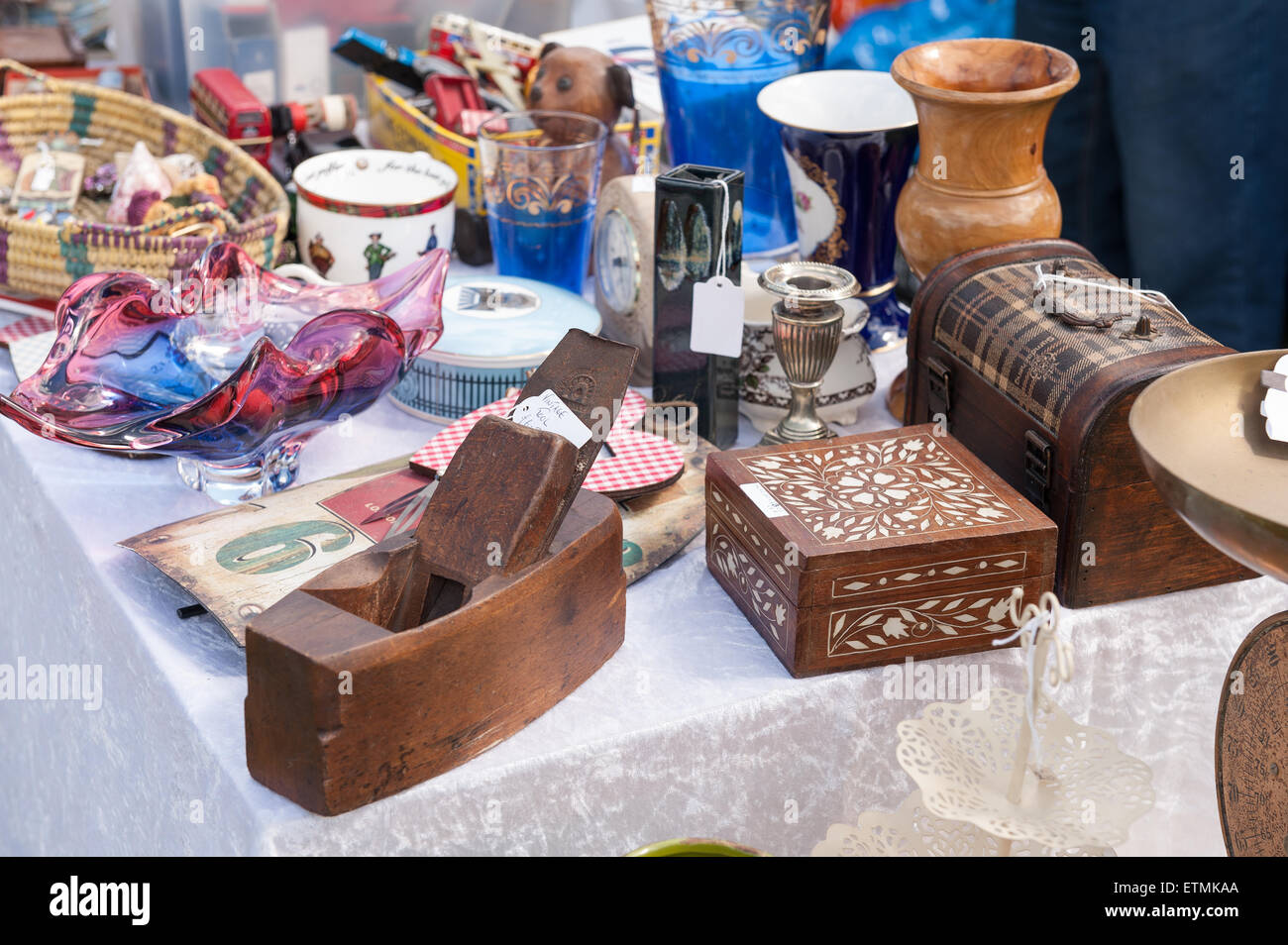 Typical display of household items for sale laid out on table at car boot fair nick knacks glasses jewelery glass wooden plane Stock Photo