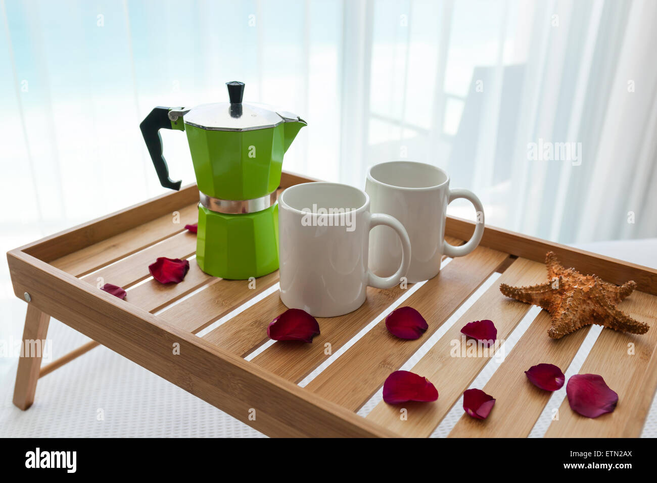 Breakfast wooden tray with coffee percolator and two cups on bed, decorated roses petals Stock Photo
