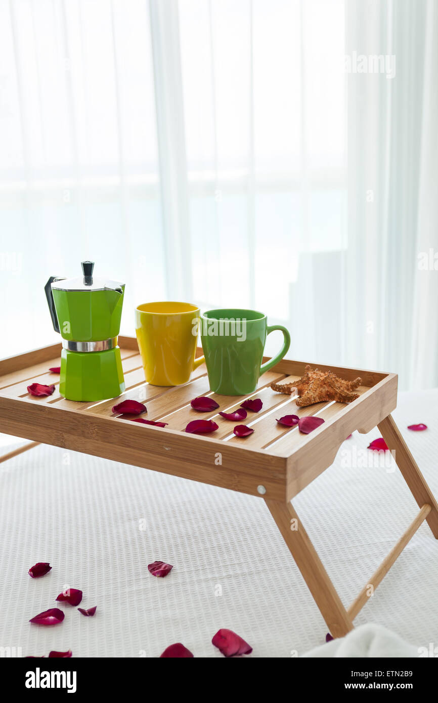 Breakfast wooden tray with coffee percolator and two cups on bed, decorated roses petals Stock Photo