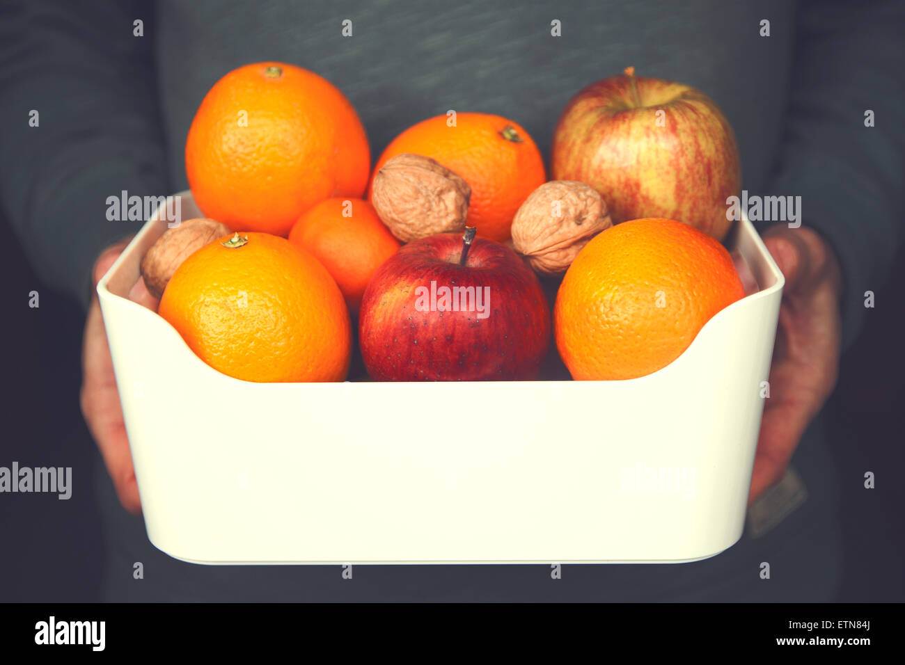 Close-up of a man holding a bowl of apples, oranges and  walnuts Stock Photo