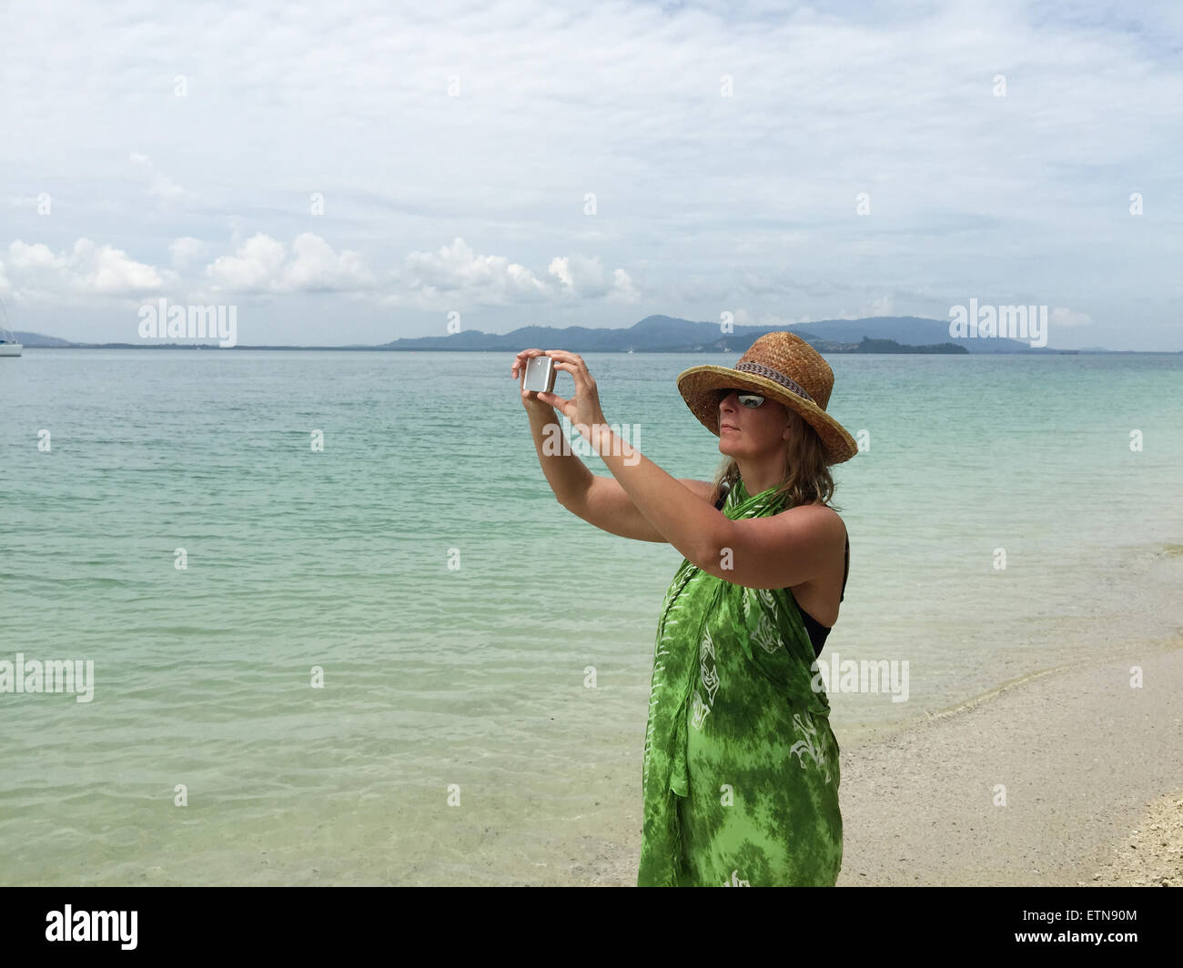 Woman standing on beach taking a photo, Phuket, Thailand Stock Photo