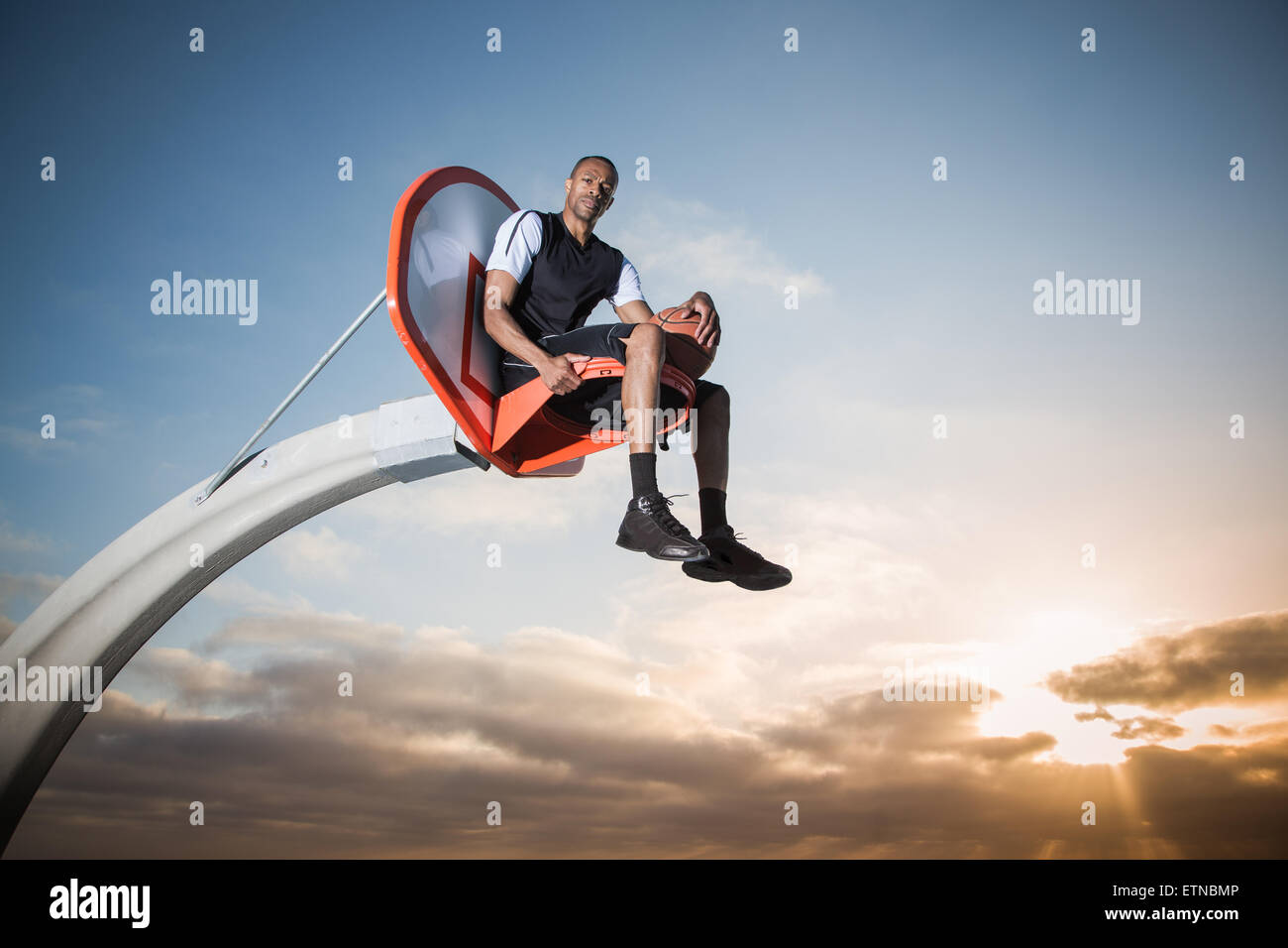 Portrait of a young man sitting in a basketball hoop in a park, Los Angeles, California, USA Stock Photo
