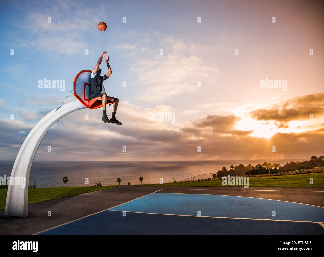Young man sitting in a basketball hoop in a park, Los Angeles, California, USA Stock Photo