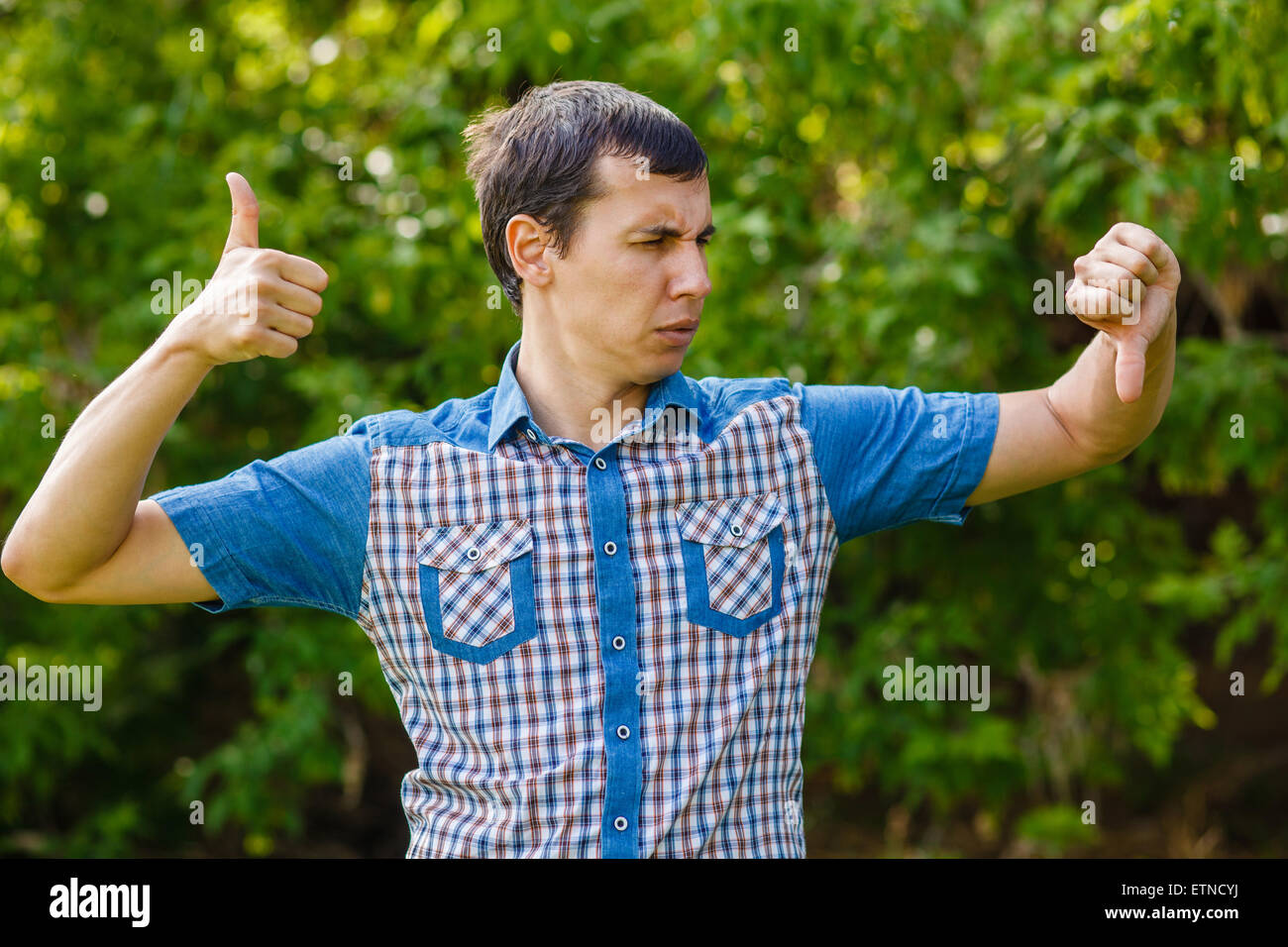 Man outdoors thumbs up thumbs down on a green background leaves Stock Photo
