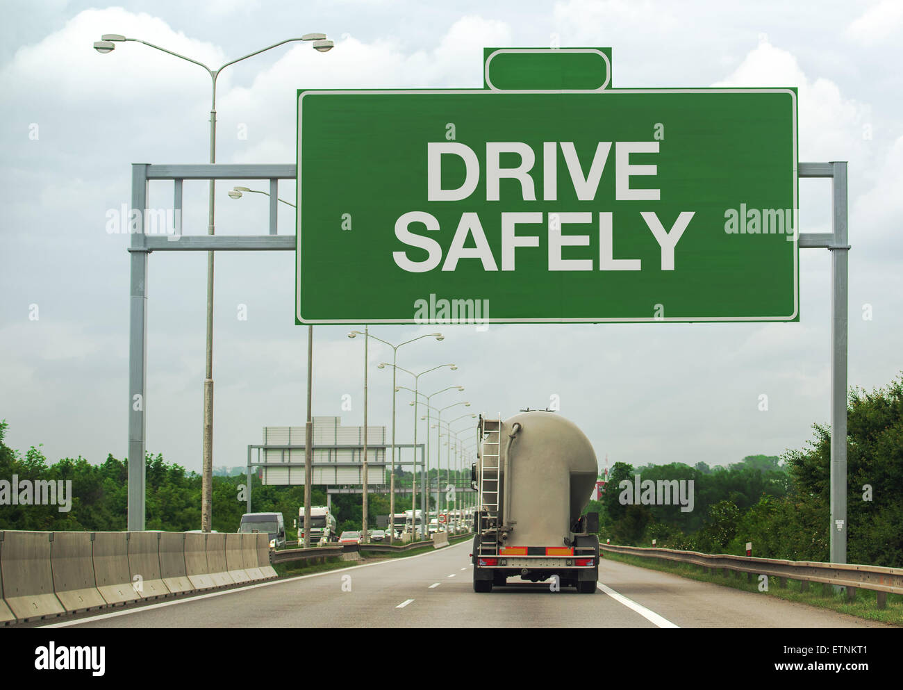 Fuel Tanker Truck on Highway Road Passing by Drive Safely Sign as a Reminder for Safety in Traffic Stock Photo