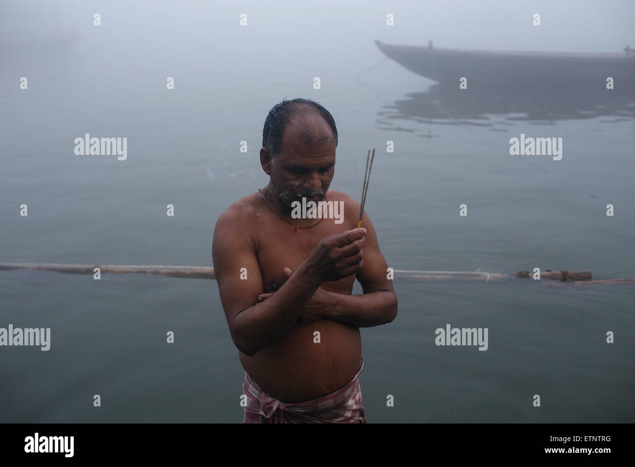 A man pilgrim praying in the misty morning in the Ganges river at the ghats in Varanasi, India Stock Photo