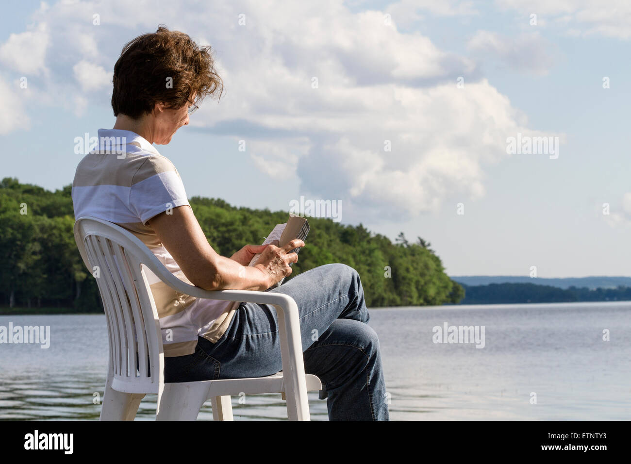 Woman sitting on a chair by the lake reading a book Stock Photo - Alamy