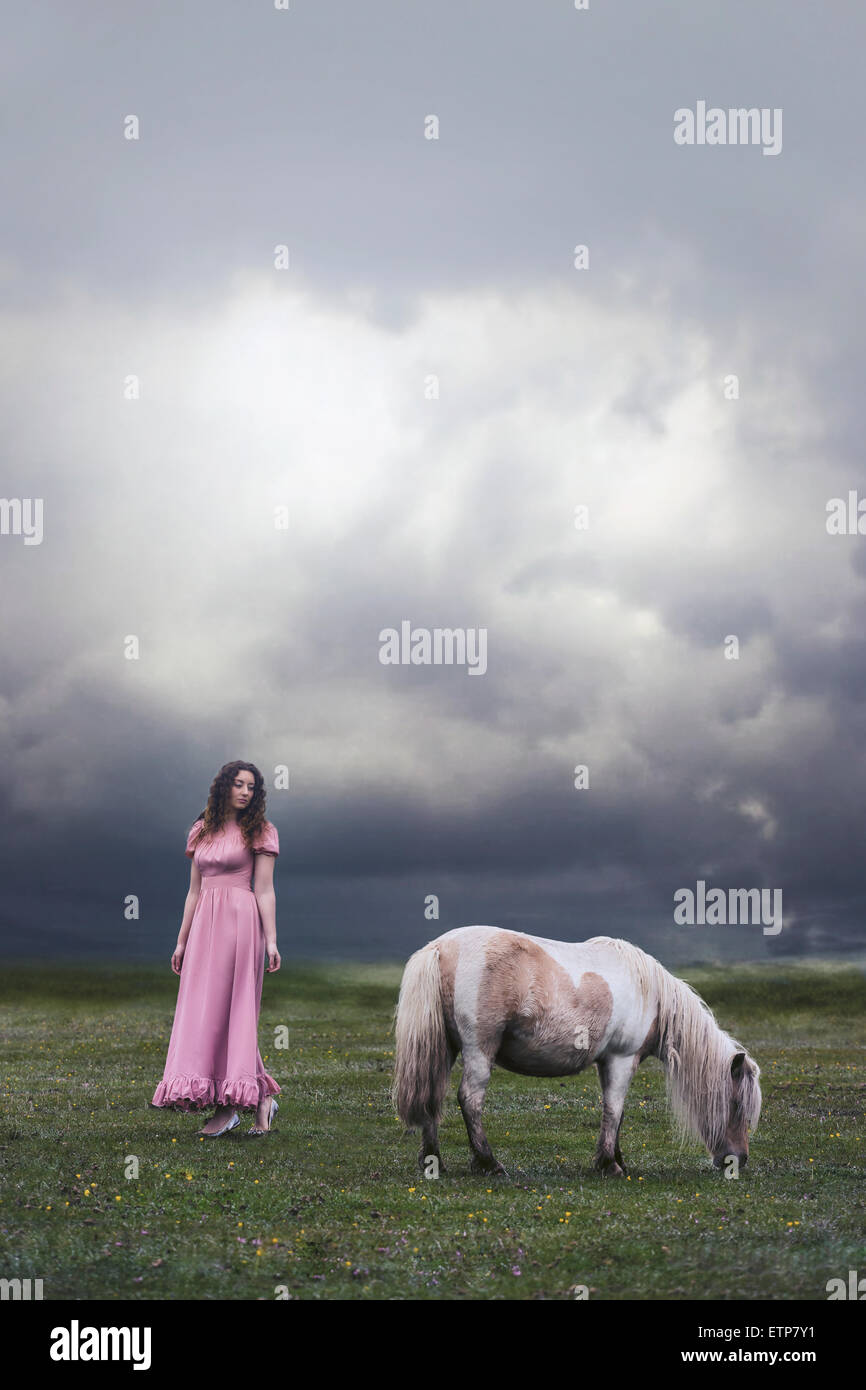 a woman in a pink dress is standing on a paddock with a pony Stock Photo