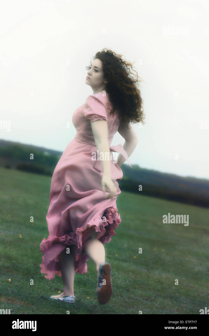 a woman in a pink dress is running on a meadow Stock Photo