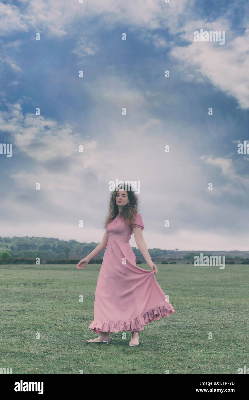 a woman in a pink dress is dancing on a meadow Stock Photo