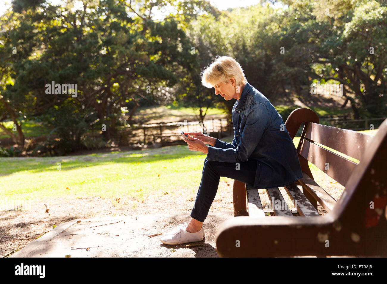 mid age woman using smart phone at the park sitting on a bench Stock Photo