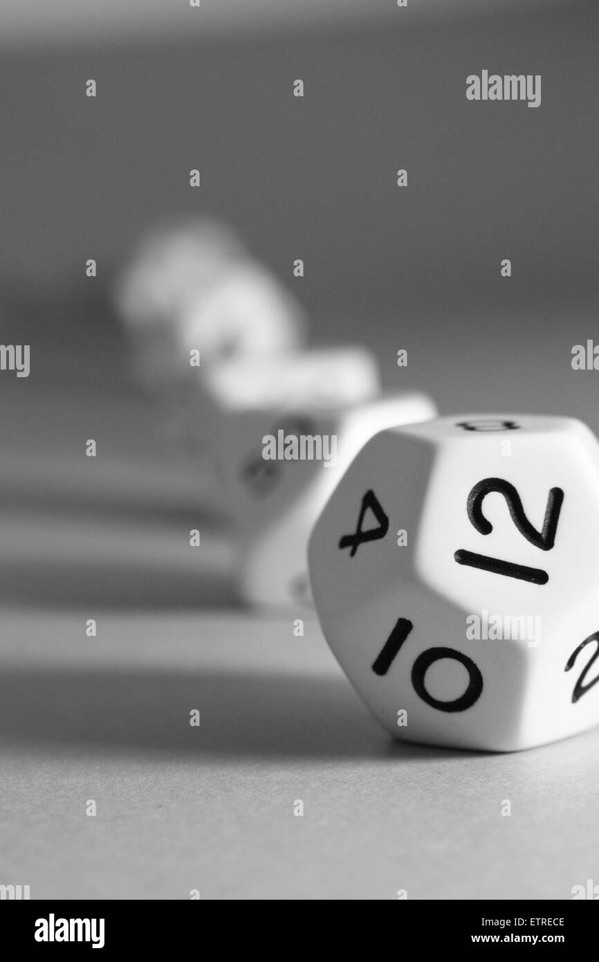 A white regular dodecahedron dice with many other shaped dice on the grey background Stock Photo