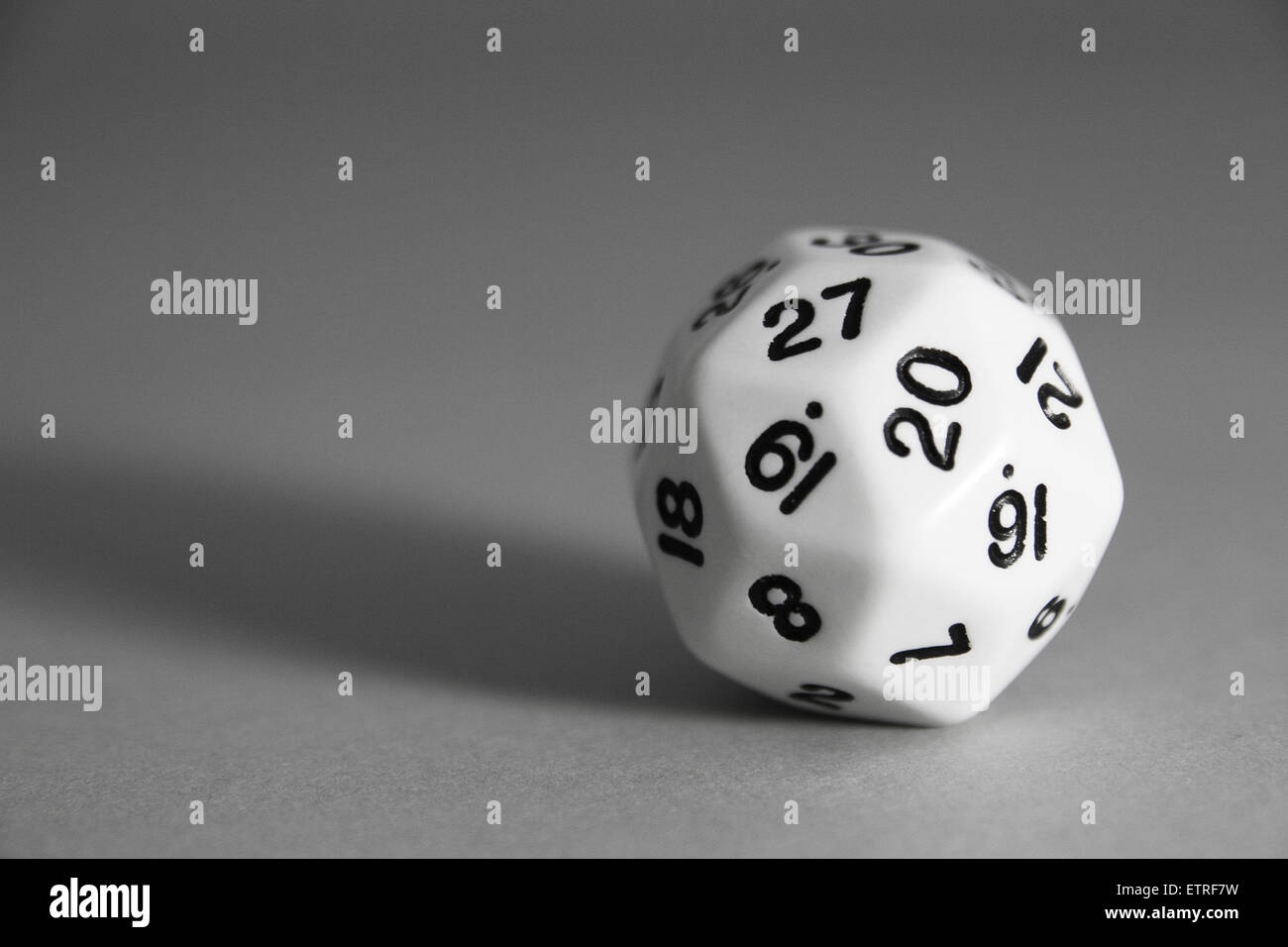 A black and white rhombic triacontahedron die on a grey background. Stock Photo