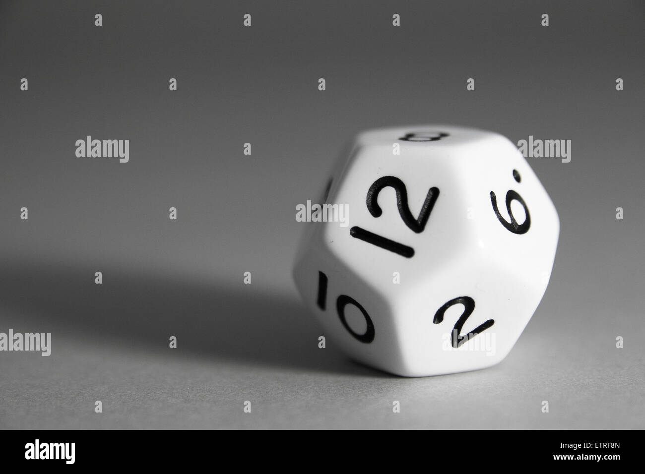 A black and white regular dodecahedron die with twelwe faces and numbers on a grey background. Stock Photo