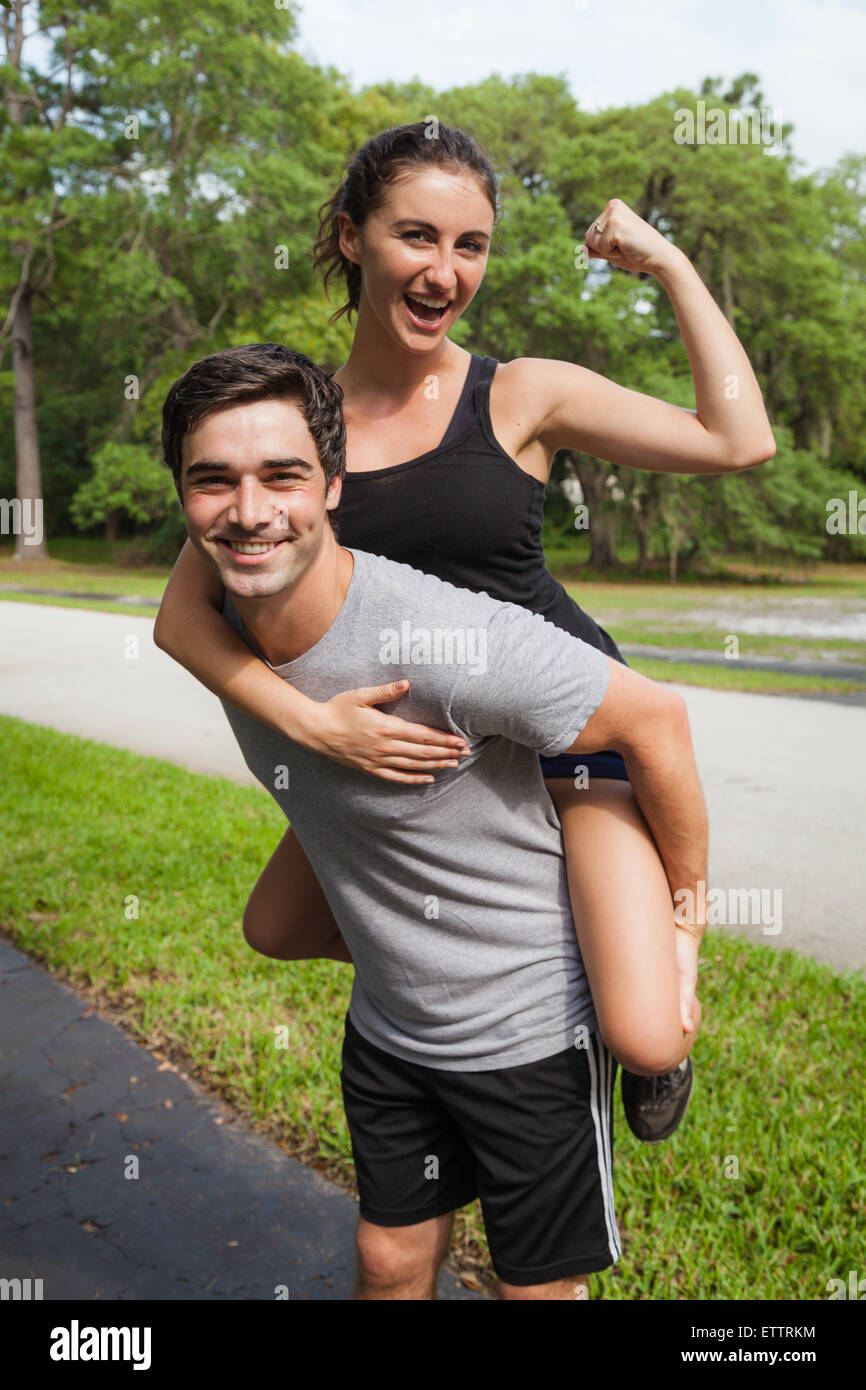 Fitness couple with female on back of male. Female is flexing and laughing while male is holding her and smiling Stock Photo