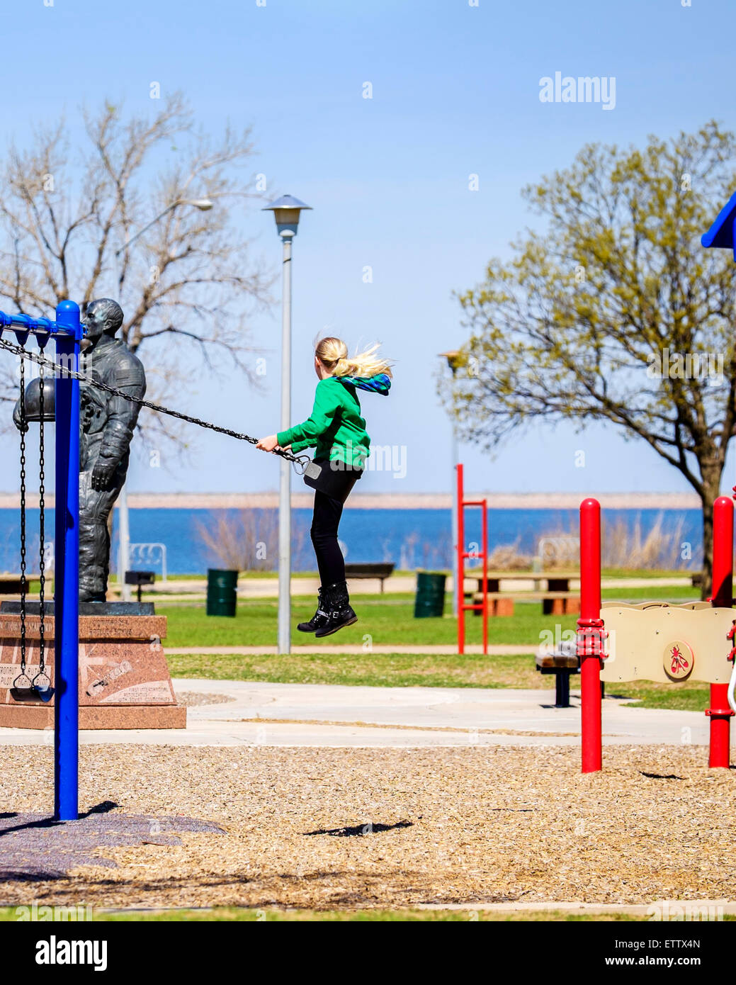 A ten year old blonde Caucasian girl soars high on a public  park swing. Stock Photo