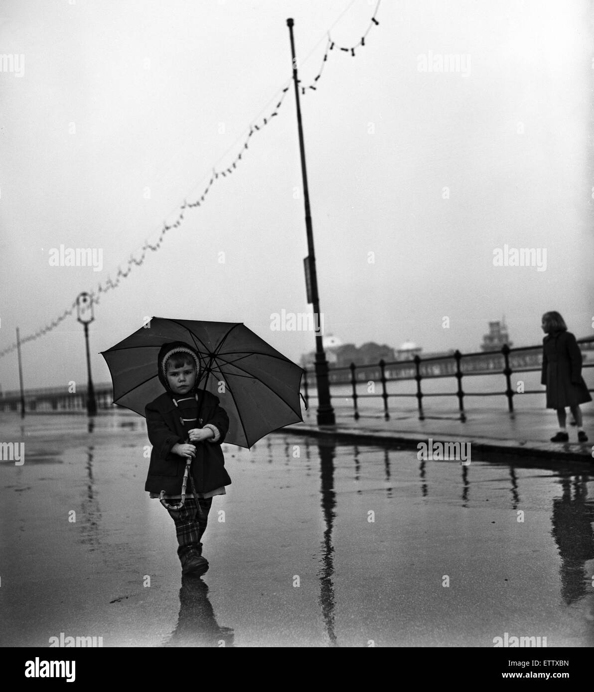 Under a large umbrella is two year old Margaret Curry of Aston, Preston, on the promenade at New Brighton, Merseyside.  1st April 1959. Stock Photo