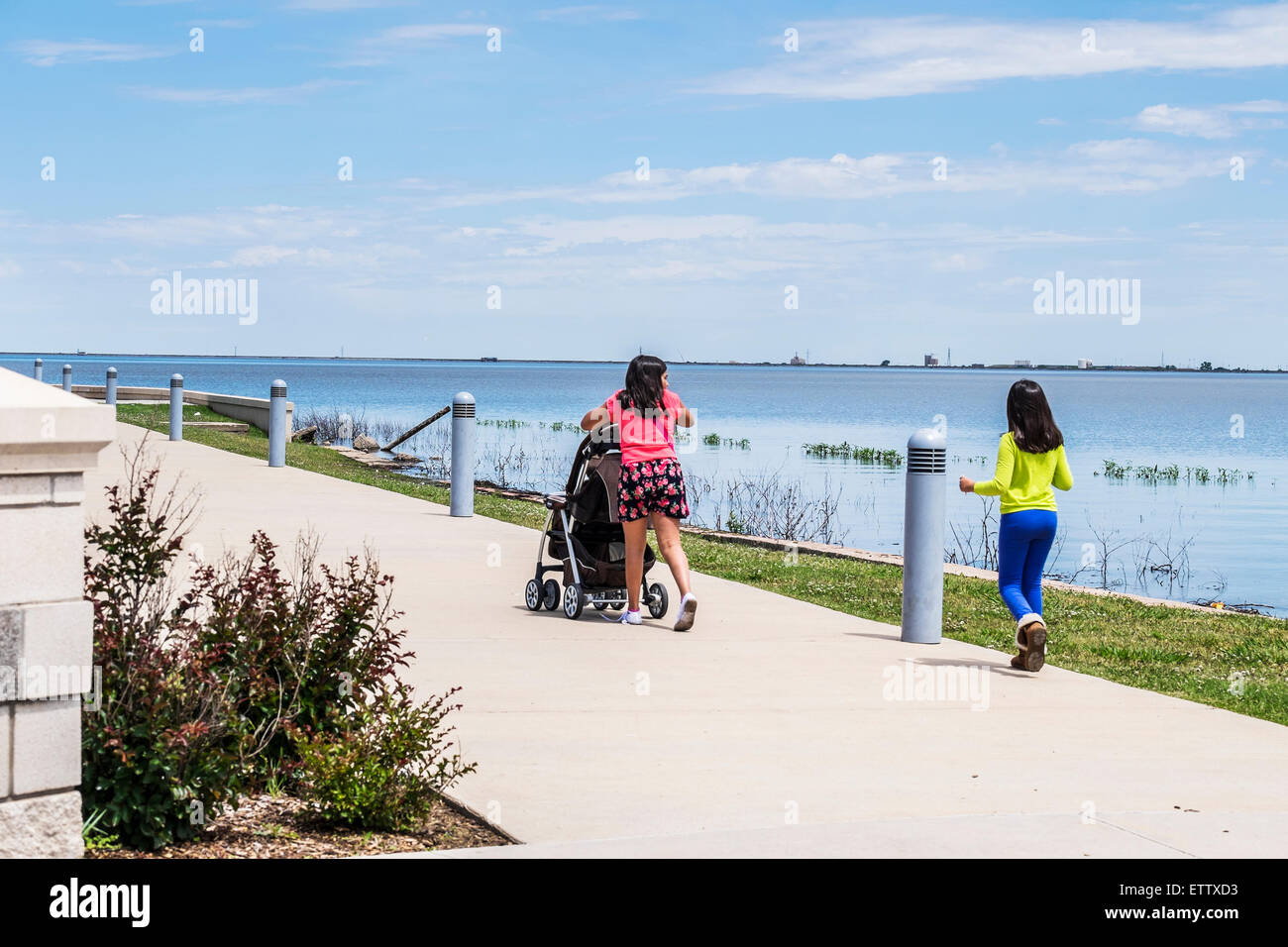 Two Hispanic girls pushing a stroller, walk toward the Eisenhower Plaza on Lake Hefner, Oklahoma City, Oklahoma, USA. Stock Photo