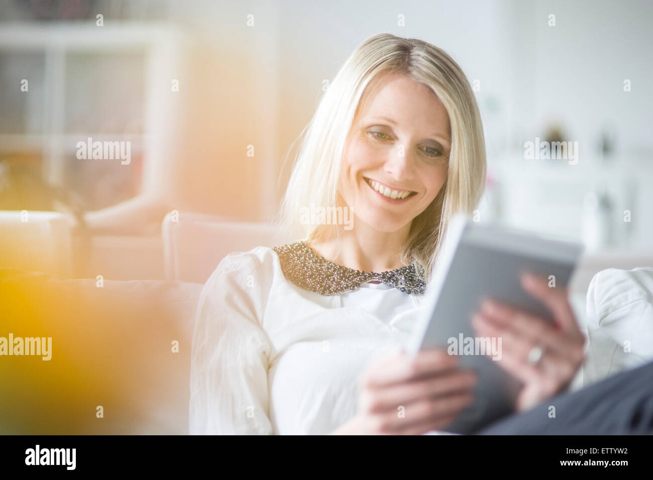 Portrait of smiling blond woman using mini tablet at home Stock Photo