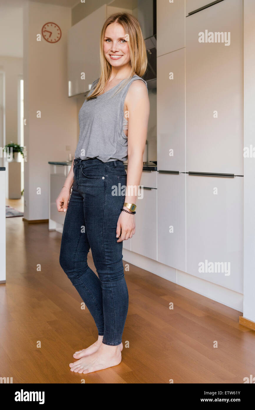 Smiling blond woman standing barefoot in a kitchen Stock Photo