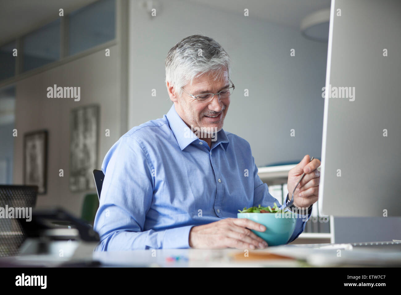 Businessman sitting at desk, eating salad Stock Photo