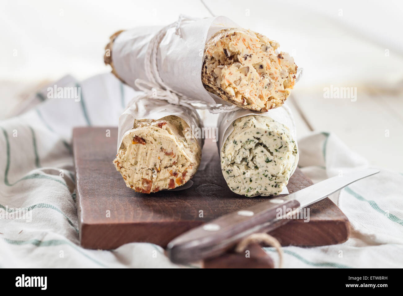 Three rolls of differently flavoured compound butters on chopping board Stock Photo