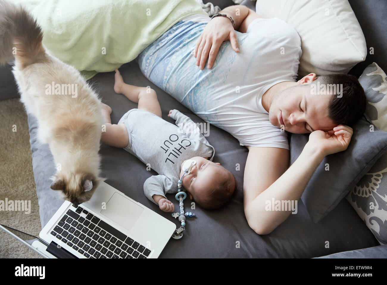 Young father and baby sleeping on couch with cat and laptop Stock Photo