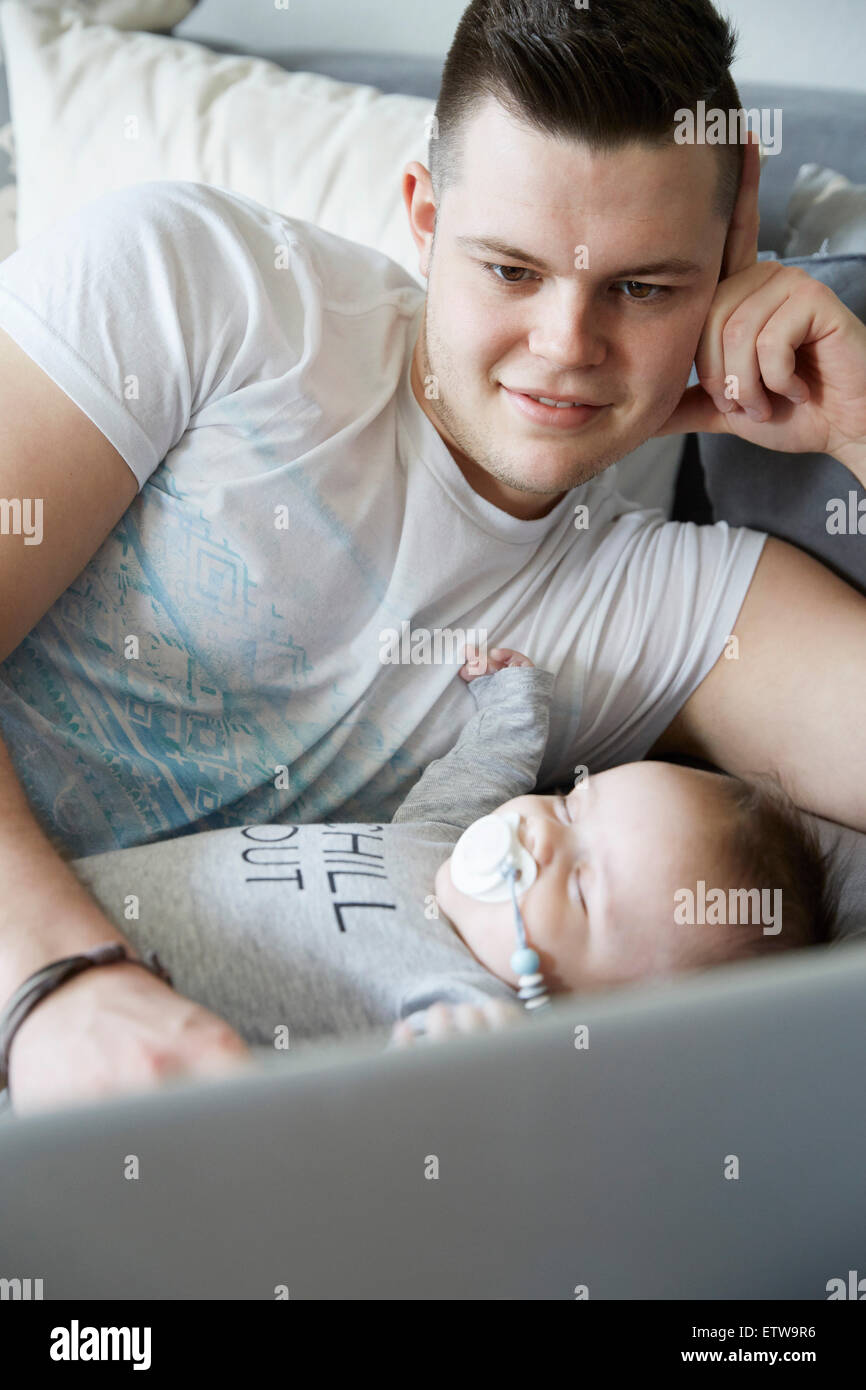 Young father using laptop with baby sleeping on couch Stock Photo Alamy