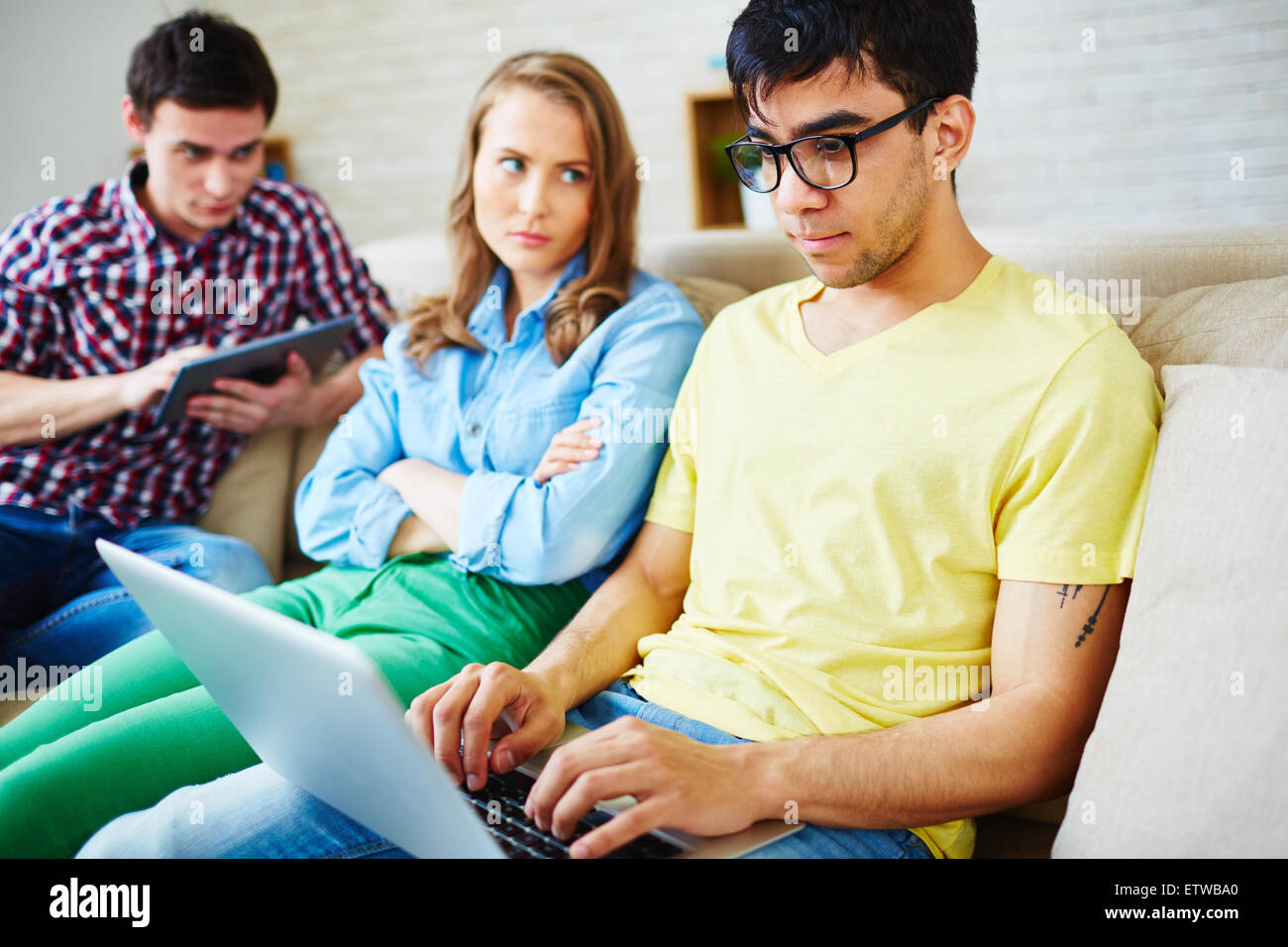 Modern teenager using laptop while his girlfriend looking at him with displeasure near by Stock Photo