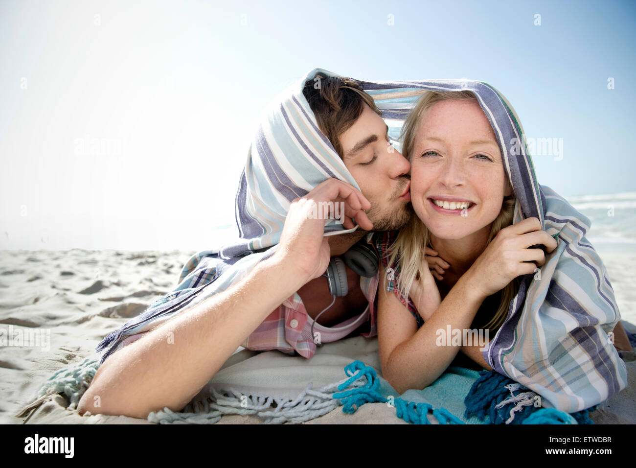 Happy young couple lying on beach kissing under a blanket Stock Photo Alamy