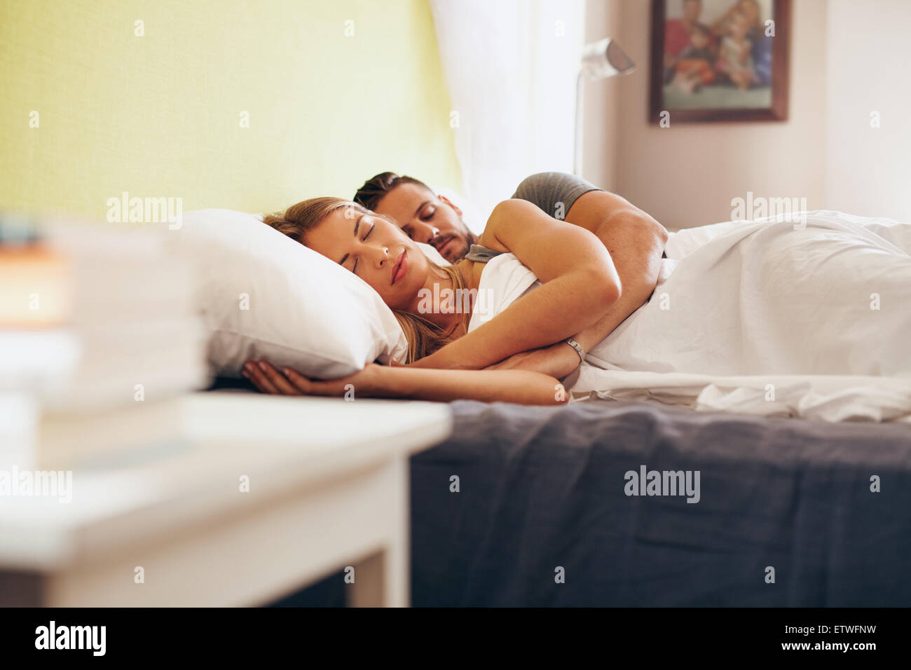 Young adult couple sleeping peacefully on the bed in bedroom. Young man embracing woman while lying asleep in bed. Stock Photo