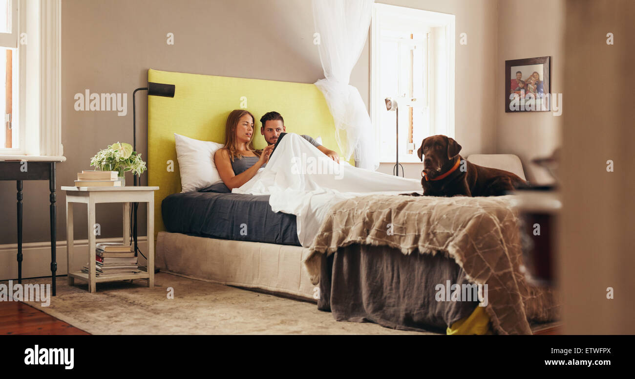 Indoor shot of young couple sharing a digital tablet while relaxing in bed at home. Couple on bed and using a digital tablet tog Stock Photo